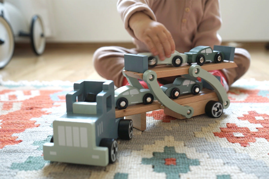 Copil incarcand masini pe rampa mobila a camionului de lemn.