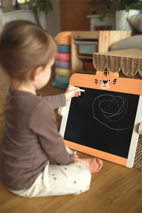 Copil desenand pe tabla alba magnetica asezata pe jos sau la masa.